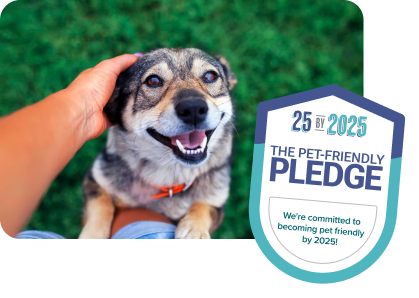 Photo of a dog leaning against a pair of legs and being pet. A Pet-Friendly Pledge badge is on top of the image